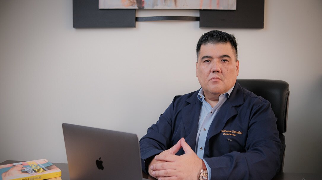 Dr. Guilherme Ghiraldini analisando um caso em seu consultório, com notebook e referências técnicas